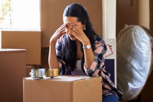 Stress, woman and moving house with headache, boxes and anxiety, tired and packing, bankrupt and debt crisis. Frustrated, female person and apartment , burnout and problem, property or mortgage loan.